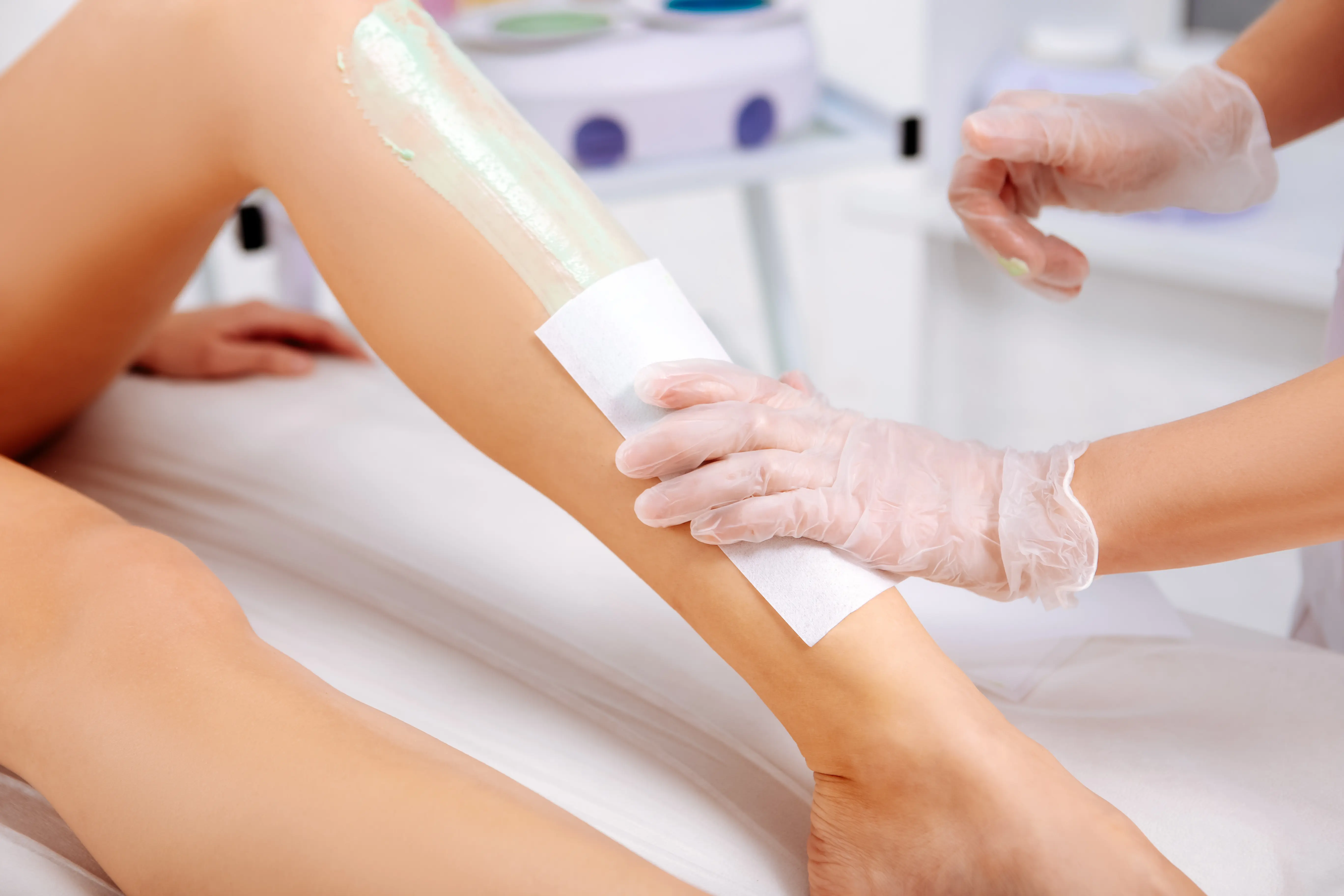 A licensed esthetician applies a waxing strip to a client’s lower leg during a professional waxing treatment at a medical spa.